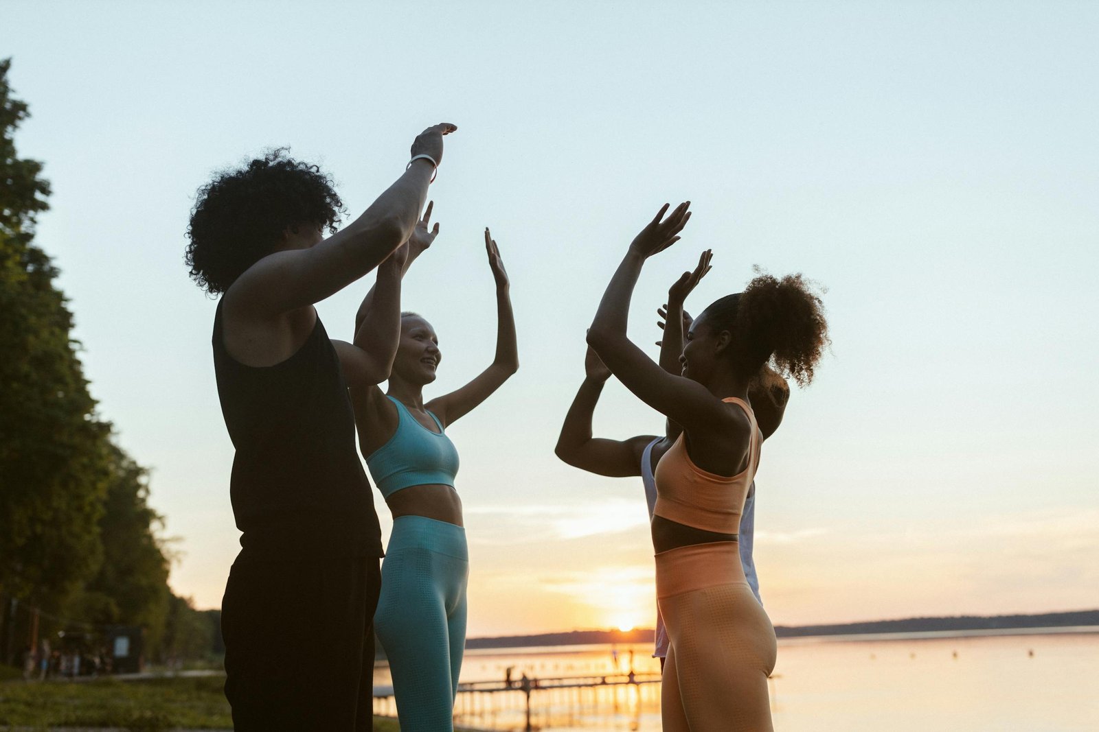 A diverse group of friends enjoying a workout by the lake at sunset, promoting a healthy lifestyle.