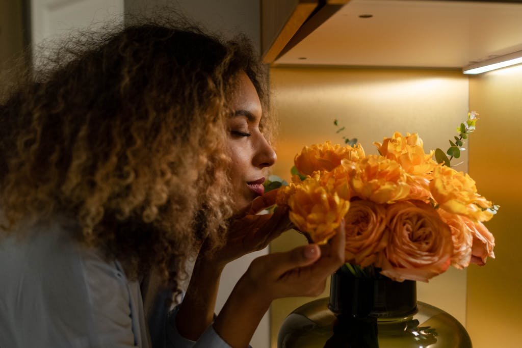 Young woman smelling a bouquet of bright orange roses in a cozy indoor setting.