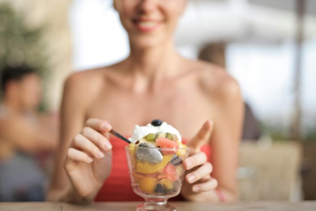 Happy woman eating fruit salad at a cafe, enjoying a refreshing dessert.